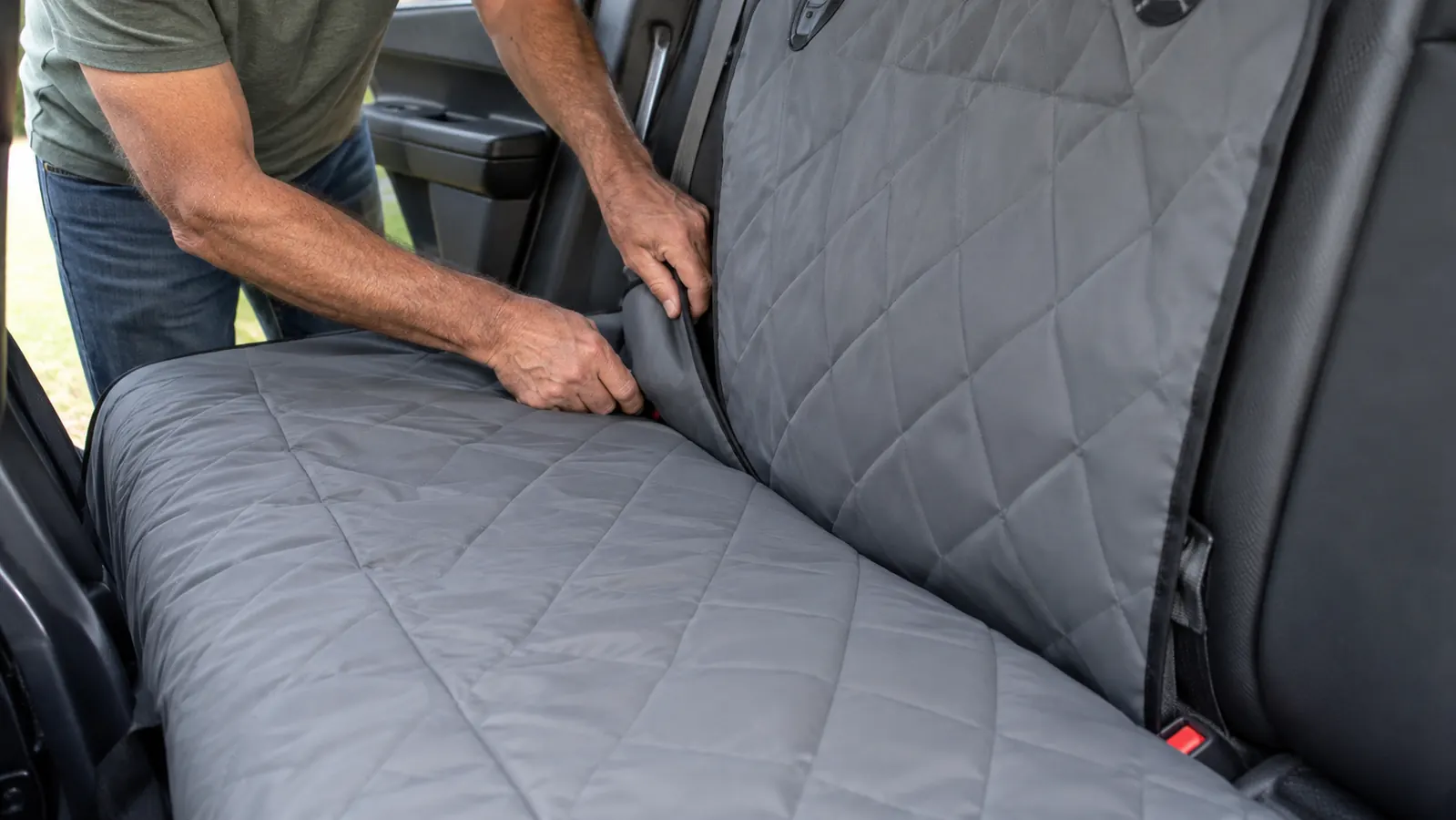 A hand tucking the edge of a hammock seat cover between the rear seat cushion and the seatback to block the gap